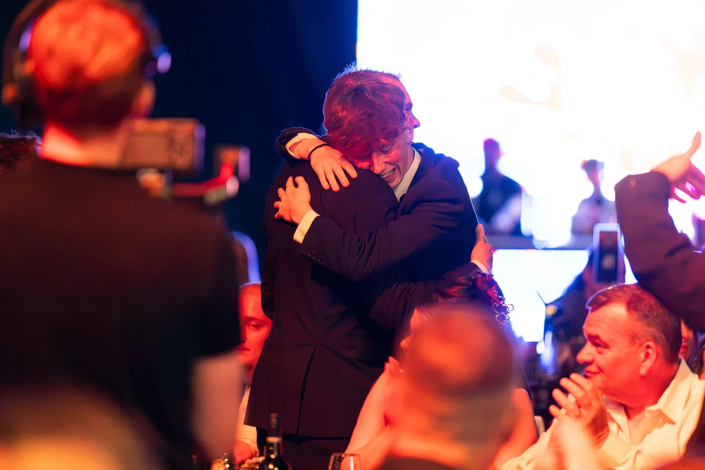 Two people embrace in the audience at the Great British Pub Awards as the table around them applauds